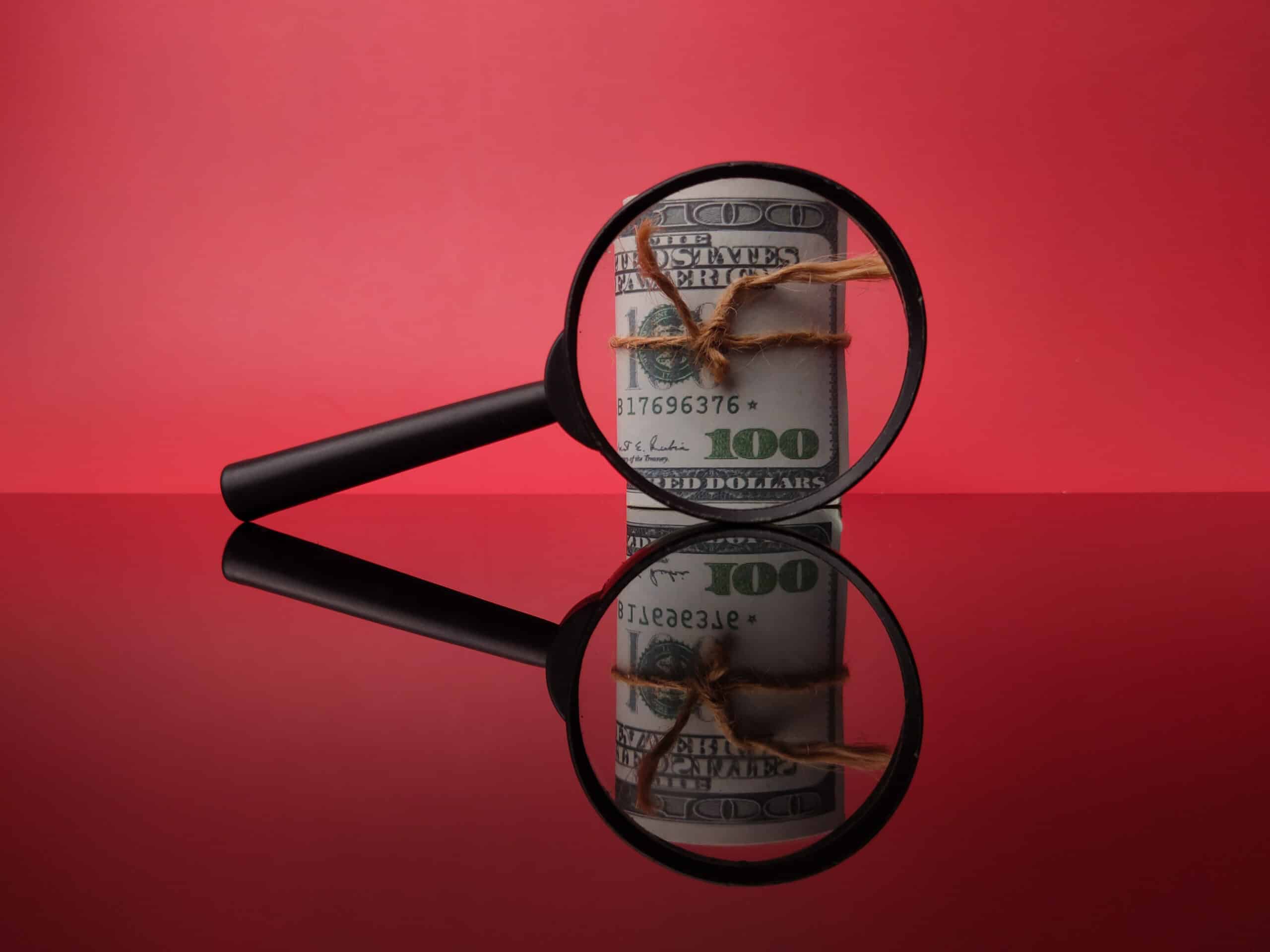 Black magnifying glass and banknotes on a red background